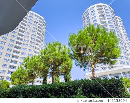 Tall buildings stand beside green trees in a bright blue sky during the day at a modern residential area Tall buildings stand beside green trees in a bright blue sky during the day at a modern residential area 143158694