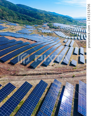 Solar panel farm in open area showing rows of solar panels under clear sky with distant hills in background Solar panel farm in open area showing rows of solar panels under clear sky with distant hills in background 143158706