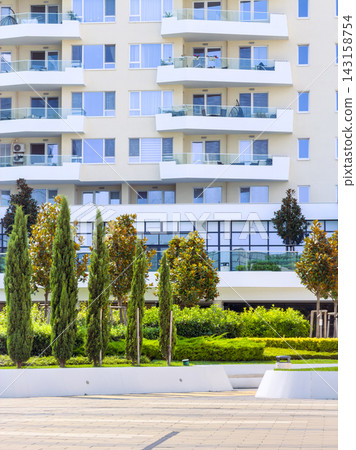 Green landscaping in front of modern apartment building during daytime with clear sky Green landscaping in front of modern apartment building during daytime with clear sky 143158754