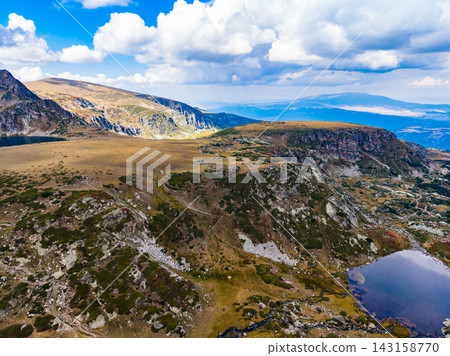 Landscape of rocky hills and a small pond in a mountain region with clouds in the sky during daytime Landscape of rocky hills and a small pond in a mountain region with clouds in the sky during daytime 143158770