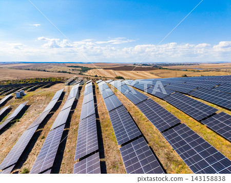 Solar panels cover a large area in a renewable energy farm near a rural landscape under a clear blue sky 143158838