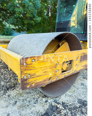 Construction equipment is parked at a work site with a yellow roller on a gravel surface in a city area during the day 143158840
