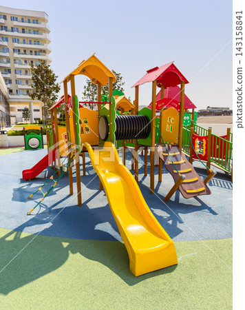 Playground with slides, climbing structures, and activity panels in a bright area with buildings in the background Playground with slides, climbing structures, and activity panels in a bright area with buildings in the background 143158841