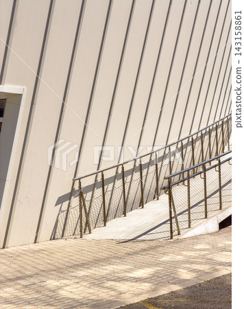 Modern ramp near building with diagonal lines and shadows on bright surface during daytime Modern ramp near building with diagonal lines and shadows on bright surface during daytime 143158861