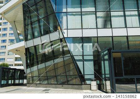 Modern building with large glass windows and unique angles in a city setting during the day Modern building with large glass windows and unique angles in a city setting during the day 143158862