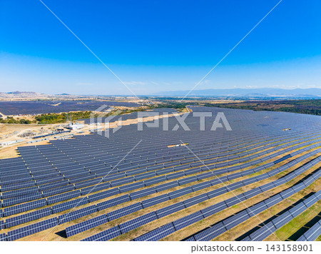 Large solar farm spreads across a vast landscape under a clear blue sky with mountains in the background and green fields around Large solar farm spreads across a vast landscape under a clear blue sky with mountains in the background and green fields around 143158901
