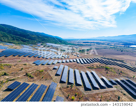 Solar panels cover a large field in a rural area with mountains in the background under a clear blue sky Solar panels cover a large field in a rural area with mountains in the background under a clear blue sky 143159042