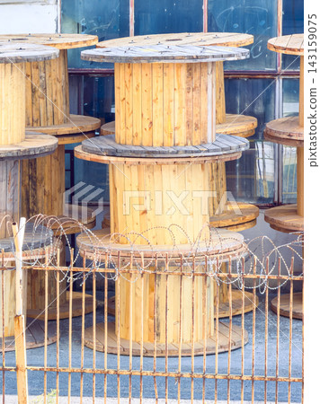 Wooden spools arranged in a storage area near a fence with barbed wire in an industrial location Wooden spools arranged in a storage area near a fence with barbed wire in an industrial location 143159075