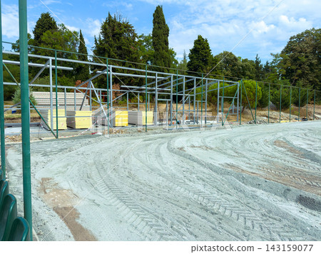 Construction of a new building structure near a park with various trees under a clear blue sky in the midday Construction of a new building structure near a park with various trees under a clear blue sky in the midday 143159077