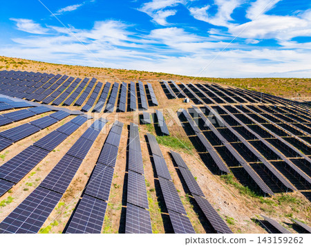 Solar panels cover a hillside in a solar farm with clear skies and few clouds in the background during daytime Solar panels cover a hillside in a solar farm with clear skies and few clouds in the background during daytime 143159262