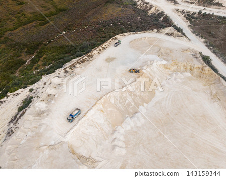 Quarry site with heavy machinery working during the day near vegetation on a hillside Quarry site with heavy machinery working during the day near vegetation on a hillside 143159344