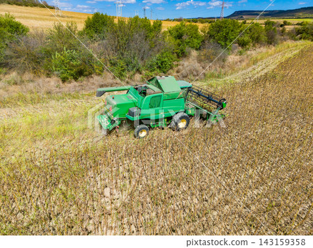 Farm equipment collects crops in a field on a bright sunny day with blue skies and distant hills in the background Farm equipment collects crops in a field on a bright sunny day with blue skies and distant hills in the background 143159358