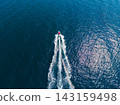 Small boat moving across water with wake and ripples in bright blue sea under clear sky 143159498