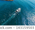 Boat moves through blue water as seagulls fly above waves near rocky shore during sunny day 143159503