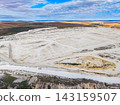 Quarry site with large open area and rough terrain during daytime under a clouded sky 143159507