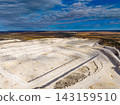 Large open quarry site with layered rock formations in a rural landscape under a blue sky 143159510