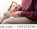 Older Person Holding Medication Bottle and Pill at Home 143159780