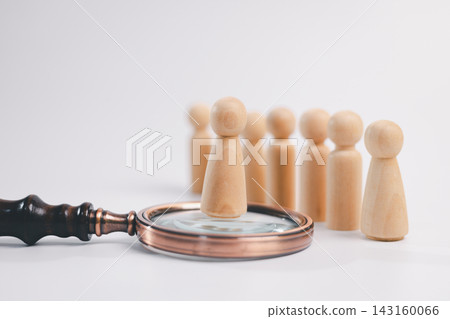 Wooden figure standing on a magnifying glass before a group, representing recruitment, candidate assessment, talent selection, hiring, leadership, human resources, evaluation, and career opportunity. Wooden figure standing on a magnifying glass before a group, representing recruitment, candidate assessment, talent selection, hiring, leadership, human resources, evaluation, and career opportunity. 143160066