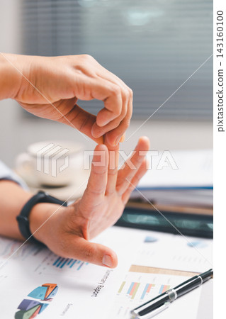 Office worker stretching fingers and open palm above business reports at desk, illustrating hand mobility, repetitive strain prevention, ergonomics, work breaks, wellness and healthy office habits. Office worker stretching fingers and open palm above business reports at desk, illustrating hand mobility, repetitive strain prevention, ergonomics, work breaks, wellness and healthy office habits. 143160100