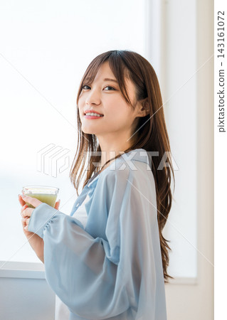 一位年輕女子早餐喝一杯綠色蔬果。這是她注重營養健康的晨間習慣。 一位年輕女子早餐喝一杯綠色蔬果。這是她注重營養健康的晨間習慣。 143161072
