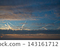 Dramatic sunset sky with layered dark clouds and illuminated airplane contrails crossing a blue and orange horizon. 143161712