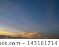 Dramatic sunset sky with layered dark clouds and illuminated airplane contrails crossing a blue and orange horizon. 143161714