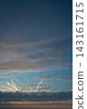 Dramatic sunset sky with layered dark clouds and illuminated airplane contrails crossing a blue and orange horizon. 143161715