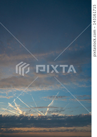 Dramatic sunset sky with layered dark clouds and illuminated airplane contrails crossing a blue and orange horizon. Dramatic sunset sky with layered dark clouds and illuminated airplane contrails crossing a blue and orange horizon. 143161715