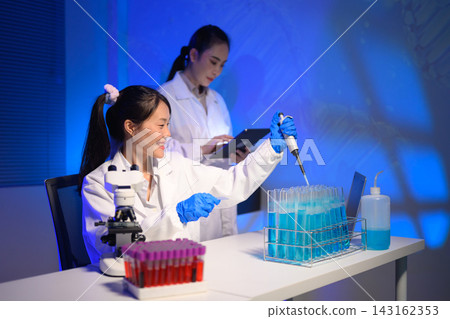 Female Scientists Working in Modern Laboratory with Pipette and Test Tubes Under Blue Light Female Scientists Working in Modern Laboratory with Pipette and Test Tubes Under Blue Light 143162353