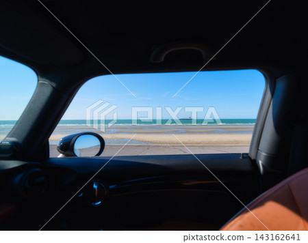 View from a car side window of a beach at low tide with a ship on the horizon. 143162641