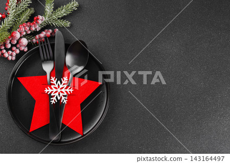 Christmas table setting with black plate and black cutlery in festive holder on dark background Christmas table setting with black plate and black cutlery in festive holder on dark background 143164497