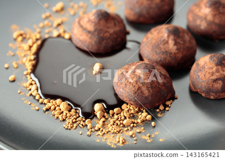 Chocolate truffles with cocoa powder and chocolate sauce on a black plate. Chocolate truffles with cocoa powder and chocolate sauce on a black plate. 143165421