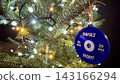 A blue weight plate ornament hangs on a Christmas tree surrounded by warm festive lights. The sporty decoration blends holiday cheer with gym inspiration, creating a unique fitness themed New Year 143166294
