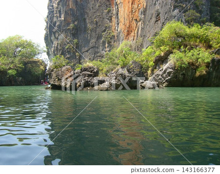The calm waters of Phang Nga Bay in Thailand reflect the rocky cliffs and lush greenery. The calm waters of Phang Nga Bay in Thailand reflect the rocky cliffs and lush greenery. 143166377