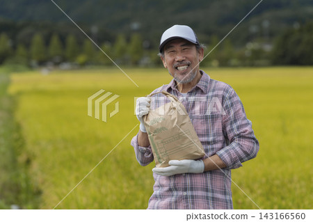 A senior man smiling and looking at the camera while holding a bag of rice. A senior man smiling and looking at the camera while holding a bag of rice. 143166560