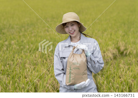 A woman smiling and looking at the camera while holding a rice bag. A woman smiling and looking at the camera while holding a rice bag. 143166731