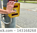 The fingertips of an elderly woman pressing a pedestrian push button. 143168268