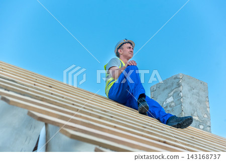 Skilled laborer takes a moment on a newly framed wooden roof under a clear blue sky, contemplating the ongoing building progress and future development of the house Skilled laborer takes a moment on a newly framed wooden roof under a clear blue sky, contemplating the ongoing building progress and future development of the house 143168737