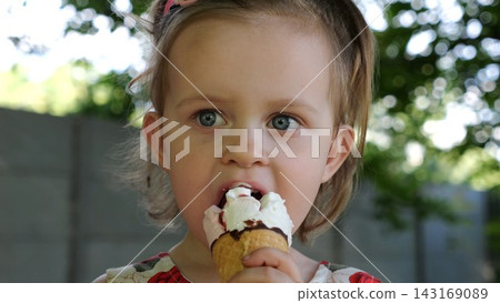 Portrait of attractive small girl eating delicious ice cream in a waffle cone outdoor. Beautiful child biting cold sweet dessert in summer garden. Cute kid enjoying tasty refreshing food on sunny day Portrait of attractive small girl eating delicious ice cream in a waffle cone outdoor. Beautiful child biting cold sweet dessert in summer garden. Cute kid enjoying tasty refreshing food on sunny day 143169089