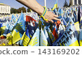 Female hand holding small flag of Ukraine and examining names of the dead war against russia. Memorial of the fallen soldiers, children, women in the center of Kyiv. Concept of tragedy and misfortune 143169202