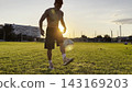 Young man juggling soccer ball on stadium at sunset. Professional footballer kicking ball at green field. Sportsman practicing tricks at meadow with sunlight at background. Freestyle football 143169203
