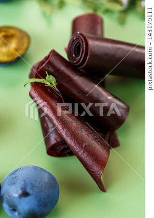 Natural fruit leather rolls with ripe blue plums on green background Natural fruit leather rolls with ripe blue plums on green background 143170111