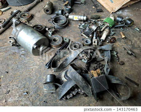 Motorcycle starter motor and assorted metal parts like bearings springs and chains scattered on dirty ground for vehicle mechanic repair and engine restoration. Motorcycle starter motor and assorted metal parts like bearings springs and chains scattered on dirty ground for vehicle mechanic repair and engine restoration. 143170463