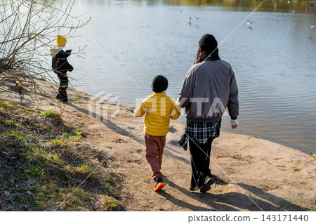 Parent and child walking hand in hand along sandy lakeshore with gulls in flight under warm autumn afternoon light, calm water reflections, and quiet outdoor nature Parent and child walking hand in hand along sandy lakeshore with gulls in flight under warm autumn afternoon light, calm water reflections, and quiet outdoor nature 143171440