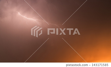 Bright Lightning Flash Against Orange Thunderstorm Sky at Sunset Bright Lightning Flash Against Orange Thunderstorm Sky at Sunset 143171585