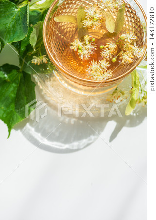 Close up of herbal linden tea in glass cup with fresh leaves and flowers refreshing beverage concept Close up of herbal linden tea in glass cup with fresh leaves and flowers refreshing beverage concept 143172810