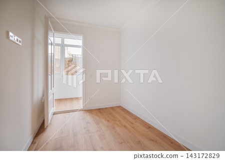 Empty room with white walls and wooden floor. A door is open, leading to a bright area with natural light. Empty room with white walls and wooden floor. A door is open, leading to a bright area with natural light. 143172829