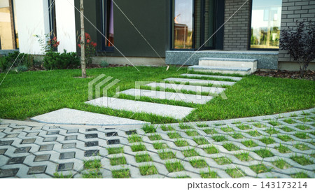 Architectural landscape showcasing modern home entrance with stepping stones and permeable pavement in lush green grass 143173214