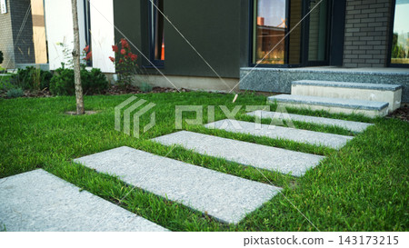 Granite stepping stones form a path across vibrant green grass, leading to a modern home that blends architecture with nature Granite stepping stones form a path across vibrant green grass, leading to a modern home that blends architecture with nature 143173215
