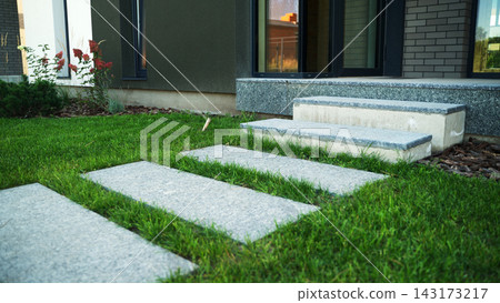 Modern building entrance with grey stepping stones pathway and green lawn leading to concrete stairs Modern building entrance with grey stepping stones pathway and green lawn leading to concrete stairs 143173217
